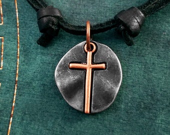 May include: A silver and copper cross pendant necklace on a black leather cord. The cross is raised and has a hammered texture.