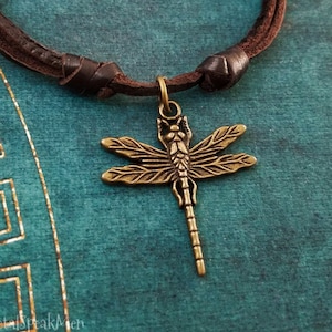 May include: A brown leather cord necklace with a gold-toned dragonfly pendant.