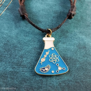 May include: A blue and gold science flask pendant necklace with a black cord. The flask design features white, gold, and blue accents, including DNA strands, an atom symbol, and a molecule. The necklace is a unique accessory.