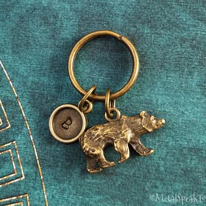 May include: A gold-toned keychain with a bear charm and a round charm with the letter "B" on it.