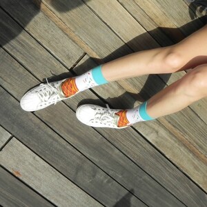 May include: A pair of white trainers with colourful ice cream cone socks. The socks have a blue background with white sprinkles and a brown ice cream cone with orange and yellow ice cream.