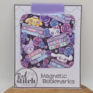 May include: A magnetic bookmark featuring a colorful pattern of cartoon characters, books, roses, and stars on a black background. The bookmark has a lavender tab and is labeled "Magnetic Bookmarks" by "Bad Stitch creations."