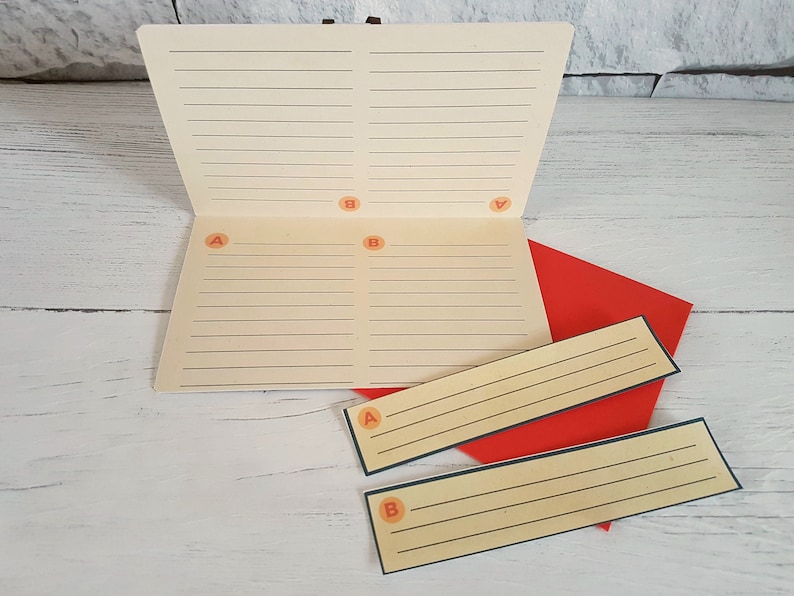 May include: A white notebook with lined pages divided into four sections labeled A and B. The notebook is open and lying on a white wooden surface. There are two smaller lined cards with A and B labels, also on the surface.