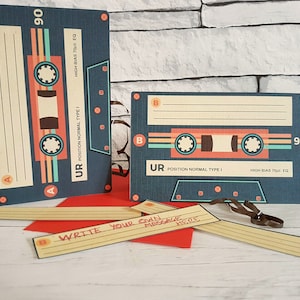 May include: Two blue and orange cassette tape cards with the text "UR POSITION NORMAL TYPE I HIGH BIAS 70US EQ" and "90". The cards are on a brick wall background. There are also several blank cards with the text "WRITE YOUR OWN MESSAGE HERE" on a wooden surface.