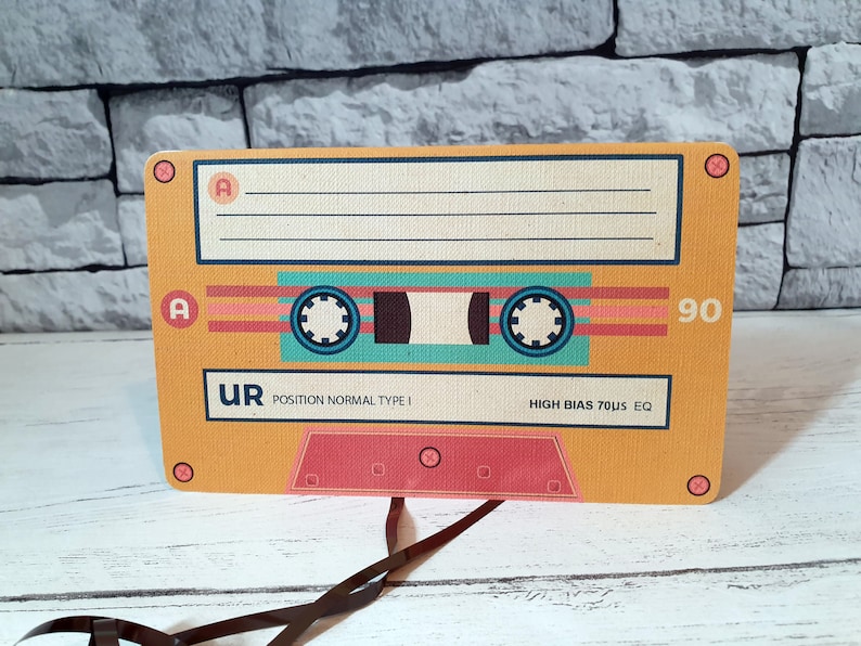May include: A yellow cassette tape with a black and blue tape reel. The tape is labeled "UR POSITION NORMAL TYPE I HIGH BIAS 70uS EQ 90".