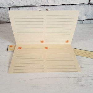 May include: A cream-colored notebook with lined pages and four orange letter stickers labeled "A" and "B".