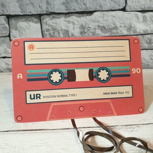 May include: A red cassette tape with the text "UR POSITION NORMAL TYPE I HIGH BIAS 70&micro;S EQ" and the number "90" printed on it.