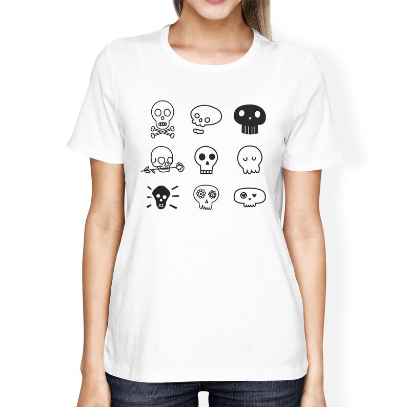 May include: White t-shirt with a black and white design of various skull illustrations. The skulls have different features, including flowers, crossbones, and eyes.