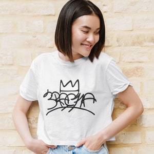 May include: A white cropped t-shirt featuring a black graphic of a crown and the word "3REYA" in a stylised font.