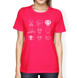 May include: A bright pink women's t-shirt with a white outline of nine different skull designs. The skulls have different features, including crossbones, flowers, and hearts.
