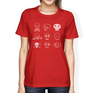May include: Red t-shirt with a white design of various skull illustrations. The skulls have different expressions and details, including flowers, crossbones, and eyes.