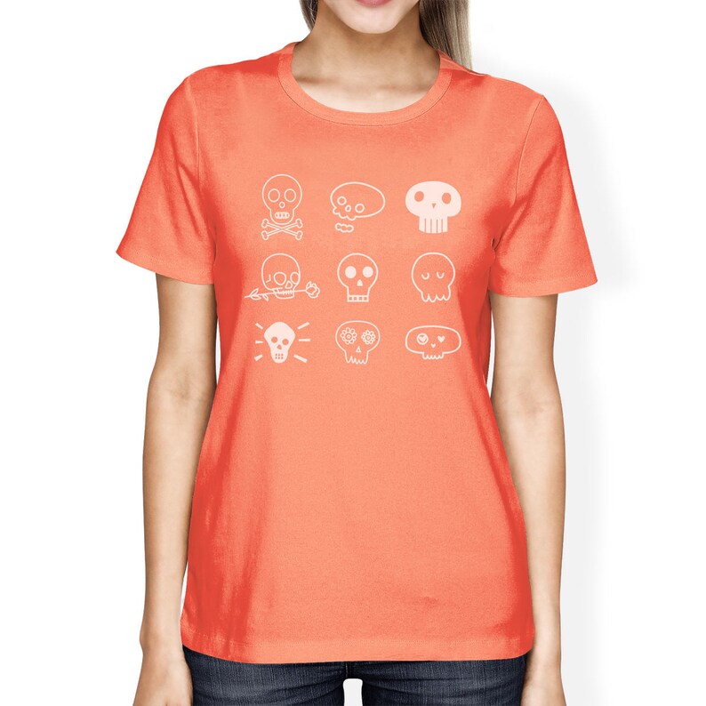 May include: A coral orange t-shirt with a white graphic of nine different skull designs. The skulls are all stylized and have different features, such as flowers, eyes, and crossbones.