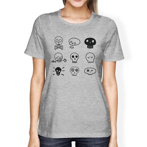 May include: Gray t-shirt with a variety of black skull designs. The skulls have different expressions and features, including crossbones, flowers, and eyes.
