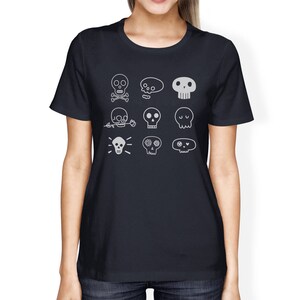 May include: A dark blue t-shirt with a white design of various skull illustrations. The skulls have different features, including crossbones, flowers, and eyes.