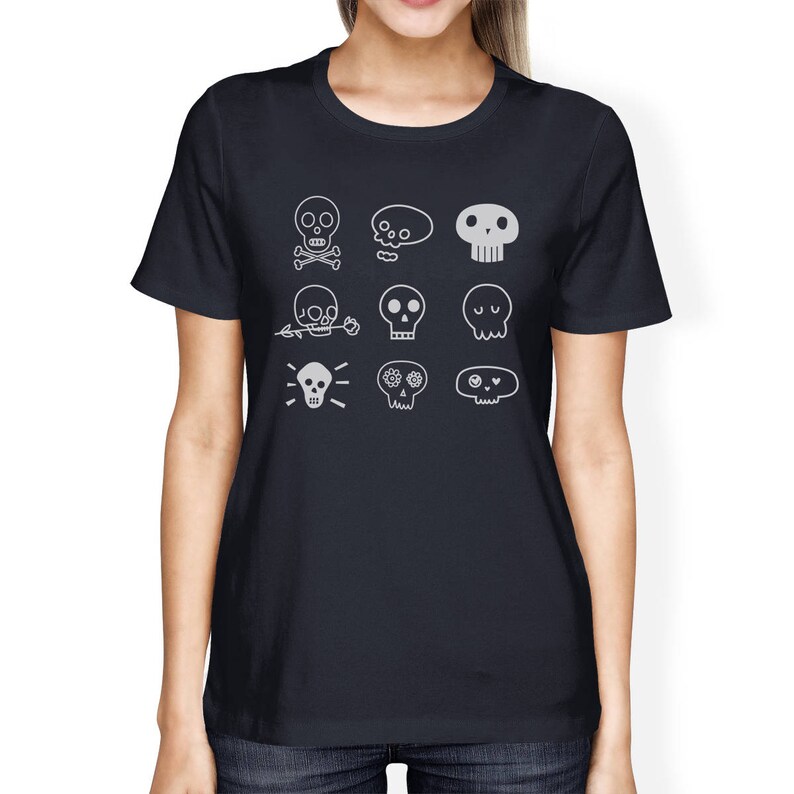 May include: A dark blue t-shirt with a white design of various skull illustrations. The skulls have different features, including crossbones, flowers, and eyes.