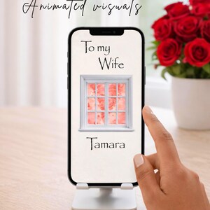 Pu&ograve; includere: Uno smartphone mostra un'immagine digitale con la scritta "To my Wife" e il nome "Tamara". L'immagine sullo schermo presenta un telaio di finestra bianco con uno sfondo rosa e rosso. Un mazzo di rose rosse &egrave; sullo sfondo.