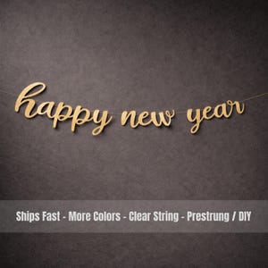 Puede incluir: Una pancarta dorada brillante de "feliz año nuevo" ensartada en una cuerda transparente. La pancarta está en una fuente cursiva y está sobre un fondo gris oscuro. El texto "Ships Fast - More Colors - Clear String - Prestrung / DIY" está en la parte inferior.