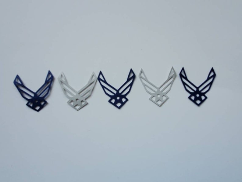 May include: Five paper cut-outs of the United States Air Force emblem. The cut-outs are in a row, with the leftmost cut-out being a solid blue colour, the next two cut-outs being a gradient of blue to white, the next cut-out being a solid white colour, and the rightmost cut-out being a solid blue colour.