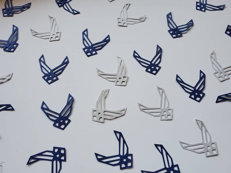 May include: A scattering of blue and white paper cutouts of the Air Force symbol. The cutouts are arranged in a random pattern on a white background.