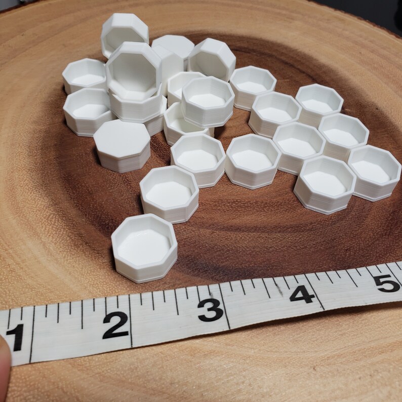 May include: A group of 20 white hexagonal plastic containers, some stacked on top of each other, on a wooden surface. A measuring tape is partially visible in the foreground.