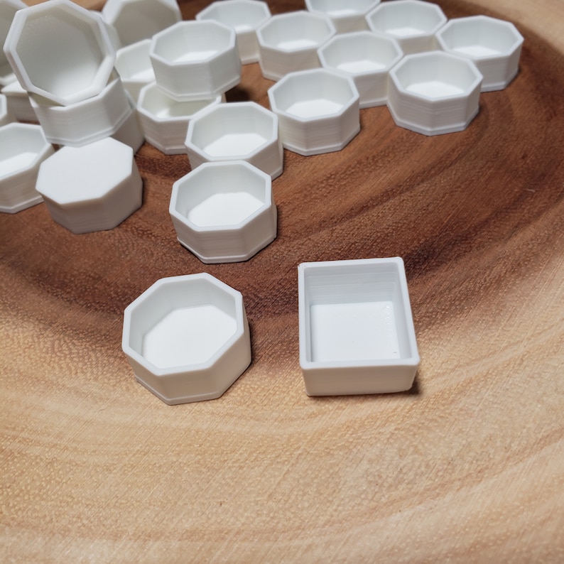 May include: A collection of white octagonal and rectangular paint palettes. The palettes are made of plastic and are arranged on a wooden surface.