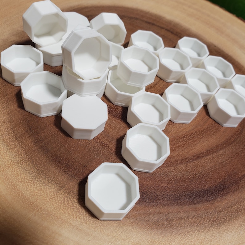 May include: A group of white octagonal containers on a wooden surface. The containers are stacked and scattered, showcasing their shape and size.