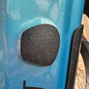 Puede incluir: Primer plano de una sección de un cuadro de bicicleta turquesa con una cubierta negra texturizada en forma ovalada. Un gráfico negro de la letra "T" es visible debajo de la cubierta. La rueda de la bicicleta es parcialmente visible en el fondo.