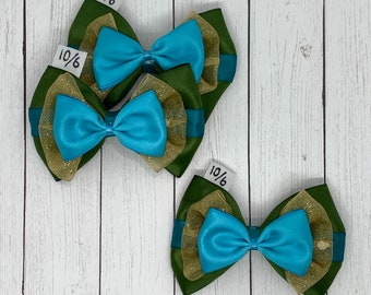 Op de afbeelding: Drie groene en gouden strik haarclips met blauwe satijnen strikken. De strikken zijn gelaagd met gouden tule en hebben een groene satijnen achterkant. De haarclips zijn gelabeld met "10/6".