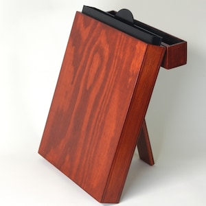 May include: A wooden box with a hinged lid and a black interior. The box is standing on a white surface and has a dark red stain.