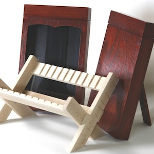 May include: Two wooden picture frames, one with a dark red finish and the other with a light wood finish, are displayed on a wooden stand. The stand has a criss-cross design and is made of light wood.