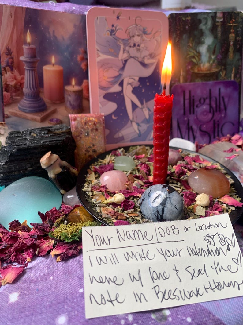 Puede incluir: Una vela roja arde en un plato negro lleno de p&eacute;talos de rosa secos, hierbas y piedras pulidas. Una tarjeta blanca en primer plano presenta un texto escrito a mano: Your Name/DOB or Location, I will write your intention here w/ love & seal the note in Beeswax Honey.
