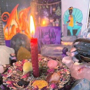 May include: A red honeycomb-textured candle burns with a bright flame, centred in a bowl filled with dried flower petals, herbs, and assorted polished gemstones. Behind the candle, three illustrated cards are displayed, including one with the text Highly Mystic.