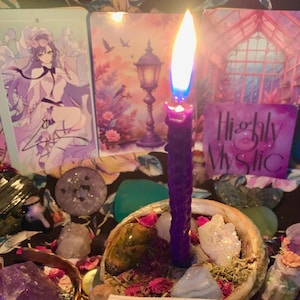 May include: A lit purple candle with a blue flame sits in a decorative shell, surrounded by crystals, dried flowers, and tarot cards. The words "Highly Mystic" are visible on a card. The scene evokes a spiritual or mystical theme.