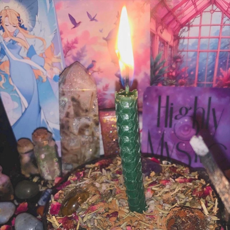Puede incluir: Una vela de cera de abeja de color verde oscuro con patr&oacute;n hexagonal y llama encendida, centrada en un cuenco lleno de hierbas secas, p&eacute;talos de flores y piedras peque&ntilde;as. La vela se mantiene erguida entre la mezcla bot&aacute;nica, emitiendo luz brillante.