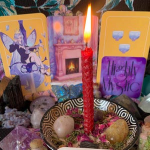 Op de afbeelding: Een brandende rode kaars in een decoratieve kom met kristallen, gedroogde kruiden en rozenblaadjes. Tarotkaarten met illustraties en de tekst "Highly Mystic" staan op de achtergrond. Mystiek thema.