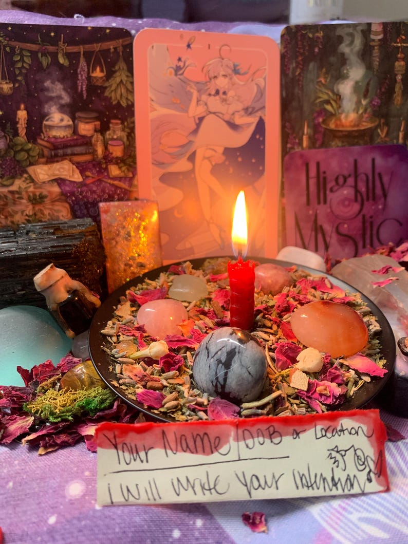 Puede incluir: Un plato negro lleno de p&eacute;talos de flores secas, hierbas y piedras pulidas alrededor de una vela roja encendida. Una nota escrita a mano al frente dice: Your Name DOB or Location I will write your intention. Cartas de tarot al fondo.