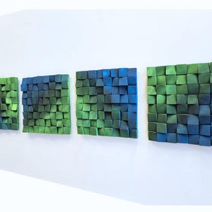 a series of three abstract artworks displayed on a white wall. Each artwork consists of a collection of small square tiles in various shades of green and blue, arranged in a grid-like pattern. The artworks are arranged in a row, creating a visually appealing and harmonious display.
