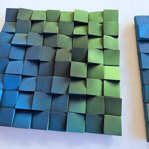 a square-shaped arrangement of small, square-shaped blocks in various shades of green and blue, creating a visually striking and textured surface.