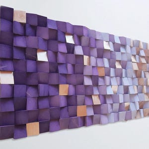 a large, abstract wall art piece composed of numerous small, square-shaped wooden blocks in various shades of purple and brown. The blocks are arranged in a grid-like pattern, creating a visually striking and textured surface.