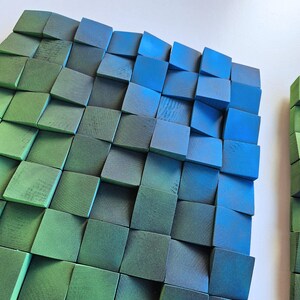a close-up view of a collection of square-shaped objects, likely composed of various materials, arranged in a grid-like pattern. The objects appear to be made of wood, with some having a green and blue color scheme. The objects are arranged in a way that they create a visually interesting and textured surface.