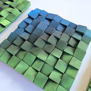 a square-shaped arrangement of green and blue wooden blocks, creating a visually striking and geometric pattern.