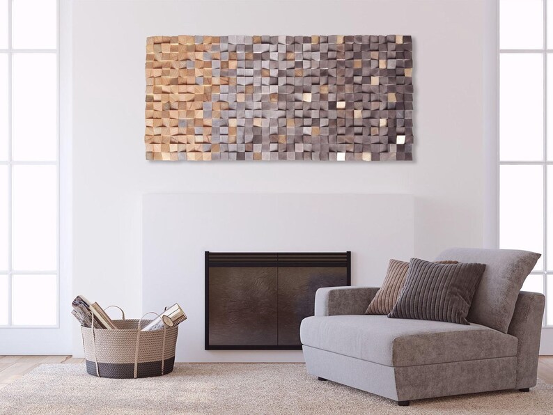 a living room with a gray sofa, a woven basket, and a fireplace. Above the fireplace, there is a large abstract art piece composed of small square tiles in various shades of brown and gray.