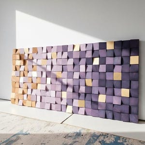a large, colorful, and abstract wall made up of numerous small square tiles in shades of purple and gold. The tiles are arranged in a grid-like pattern, creating a visually striking and dynamic display. The wall is set against a white wall, which highlights the vibrant colors and intricate design of the tiles.