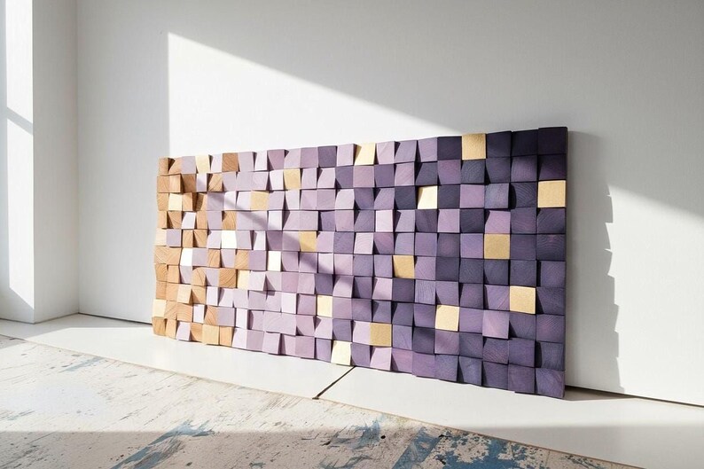 a large, colorful, and abstract wall made up of numerous small square tiles in shades of purple and gold. The tiles are arranged in a grid-like pattern, creating a visually striking and dynamic display. The wall is set against a white wall, which highlights the vibrant colors and intricate design of the tiles.