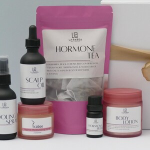 Pu&ograve; includere: Una collezione di prodotti per il benessere, tra cui uno spray rinfrescante, olio per il cuoio capelluto e lozione per il corpo, in flaconi neri e vasetti rosa. Sono presenti anche una busta rosa di Hormone Tea e una confezione regalo con un nastro dorato. I prodotti sono etichettati con il marchio.