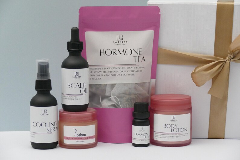 Pu&ograve; includere: Una collezione di prodotti per il benessere, tra cui uno spray rinfrescante, olio per il cuoio capelluto e lozione per il corpo, in flaconi neri e vasetti rosa. Sono presenti anche una busta rosa di Hormone Tea e una confezione regalo con un nastro dorato. I prodotti sono etichettati con il marchio.