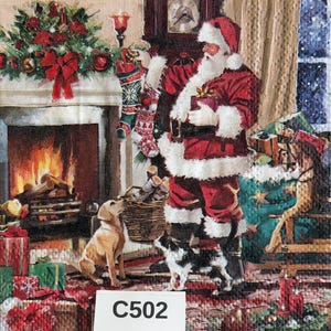 May include: A decorative napkin featuring a festive illustration of Santa Claus in a red suit hanging a stocking by a fireplace. A golden retriever and a black and white dog stand nearby. Wrapped gifts, a rocking horse, and greenery are visible.