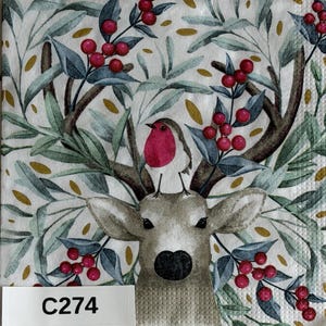 May include: A square paper napkin featuring a deer head with a small robin perched between its antlers. The design includes green leaves, gold accents, and clusters of red berries on a white background. A white label with the text C274 is visible.