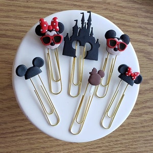 May include: Six gold paper clips with different Disney character toppers. The toppers include Mickey Mouse, Minnie Mouse, Donald Duck, Goofy, and the Disney castle.