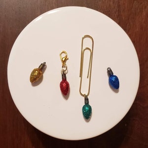 May include: Four miniature Christmas light ornaments, one gold, one red, one blue, and one green, with a gold paper clip.
